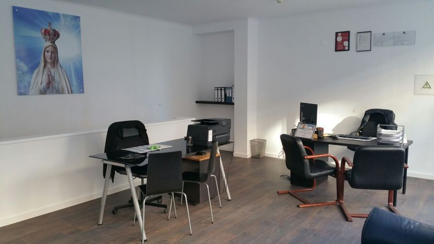 Interior de escritório com mesas, cadeiras e obras de arte religiosas na parede.