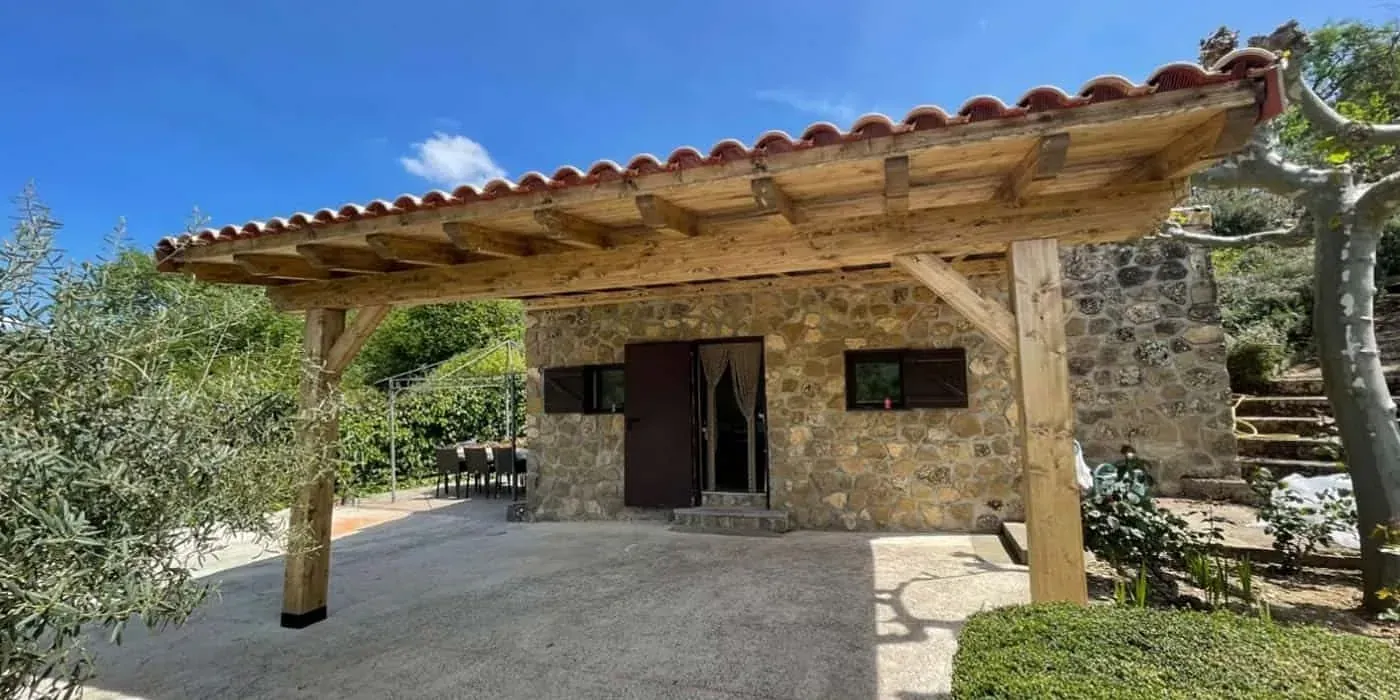 Una pequeña casa de piedra con una pérgola de madera encima.