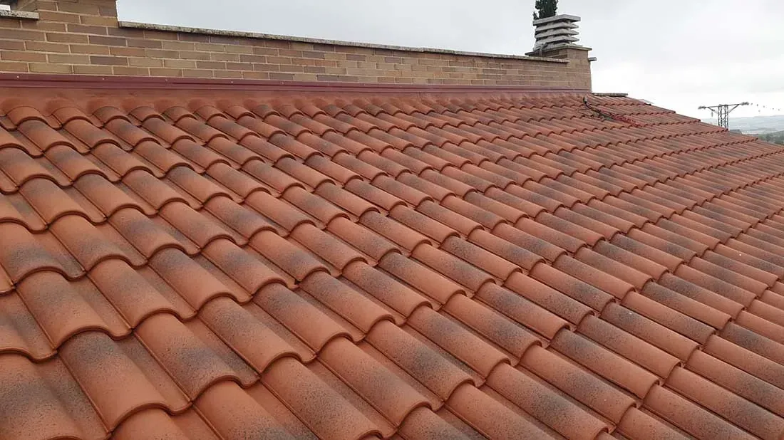 Un primer plano de un techo de tejas con una chimenea al fondo.