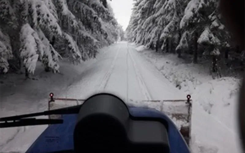 Ein Schneepflug fährt eine schneebedeckte Straße im Wald entlang.