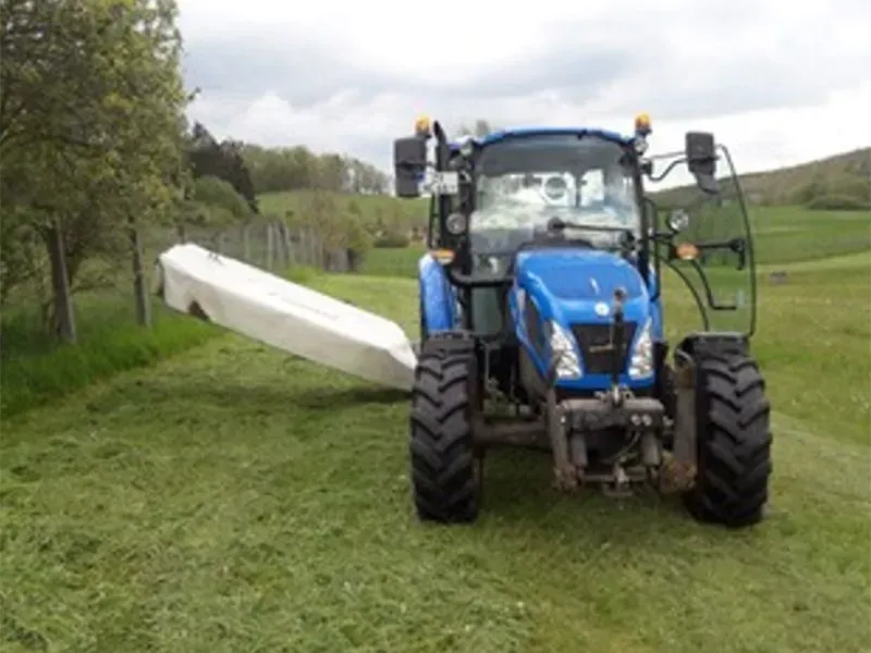 Ein blauer Traktor steht auf einer Wiese. Gala Bau & Service GbR