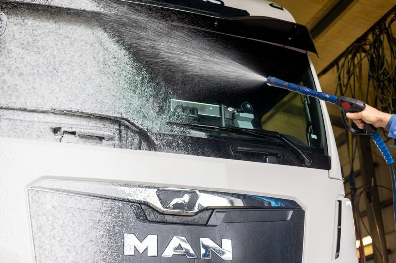 Ein Mann wäscht die Windschutzscheibe eines MAN-Lastwagens.