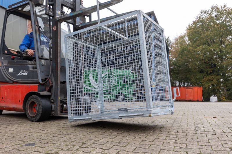 Ein Mann fährt einen Gabelstapler mit einem Käfig auf der Ladefläche.