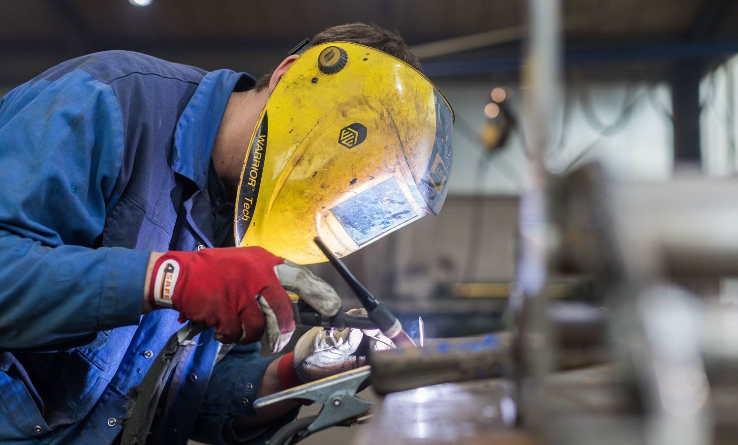 Ein Mann mit einer Schweißmaske schweißt in einer Fabrik ein Stück Metall.
