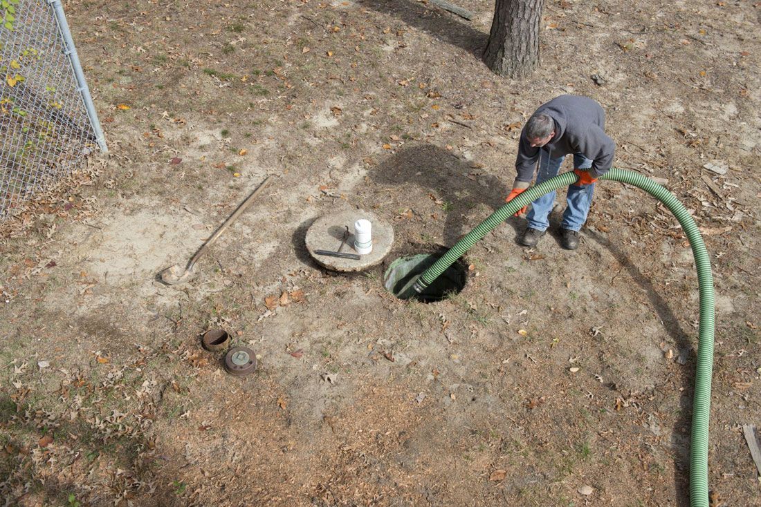 Une personne utilise un tuyau d'arrosage vert pour laver une zone de sa cour comportant une petite structure en béton.