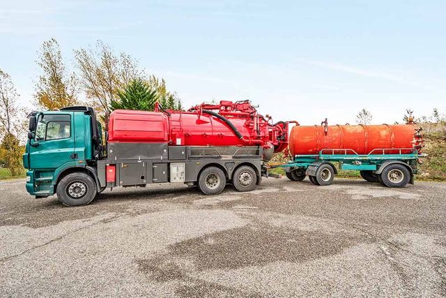 Un camion-citerne rouge tractant une remorque orange sur un parking sous un ciel dégagé