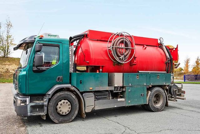 Camion aspirateur turquoise et rouge stationné en bord de route
