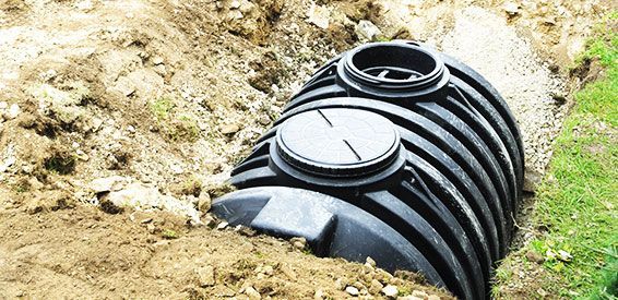 Un morceau de tuyau en plastique ondulé noir est enterré dans une tranchée de terre à côté de l'herbe.