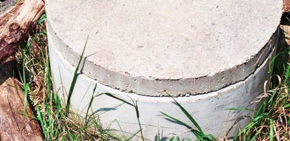 Gros plan sur le socle en béton fissuré d'un boîtier électrique, entouré d'herbe et de terre.