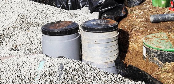 Deux tuyaux de service gris avec des bouchons noirs à côté de gravier et de terre sur un chantier de construction