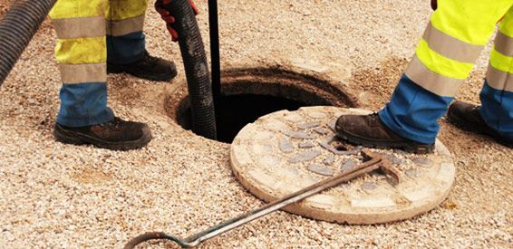 Des ouvriers portant des pantalons réfléchissants utilisent un câble près d'une bouche d'égout ouverte sur un chantier de voirie.