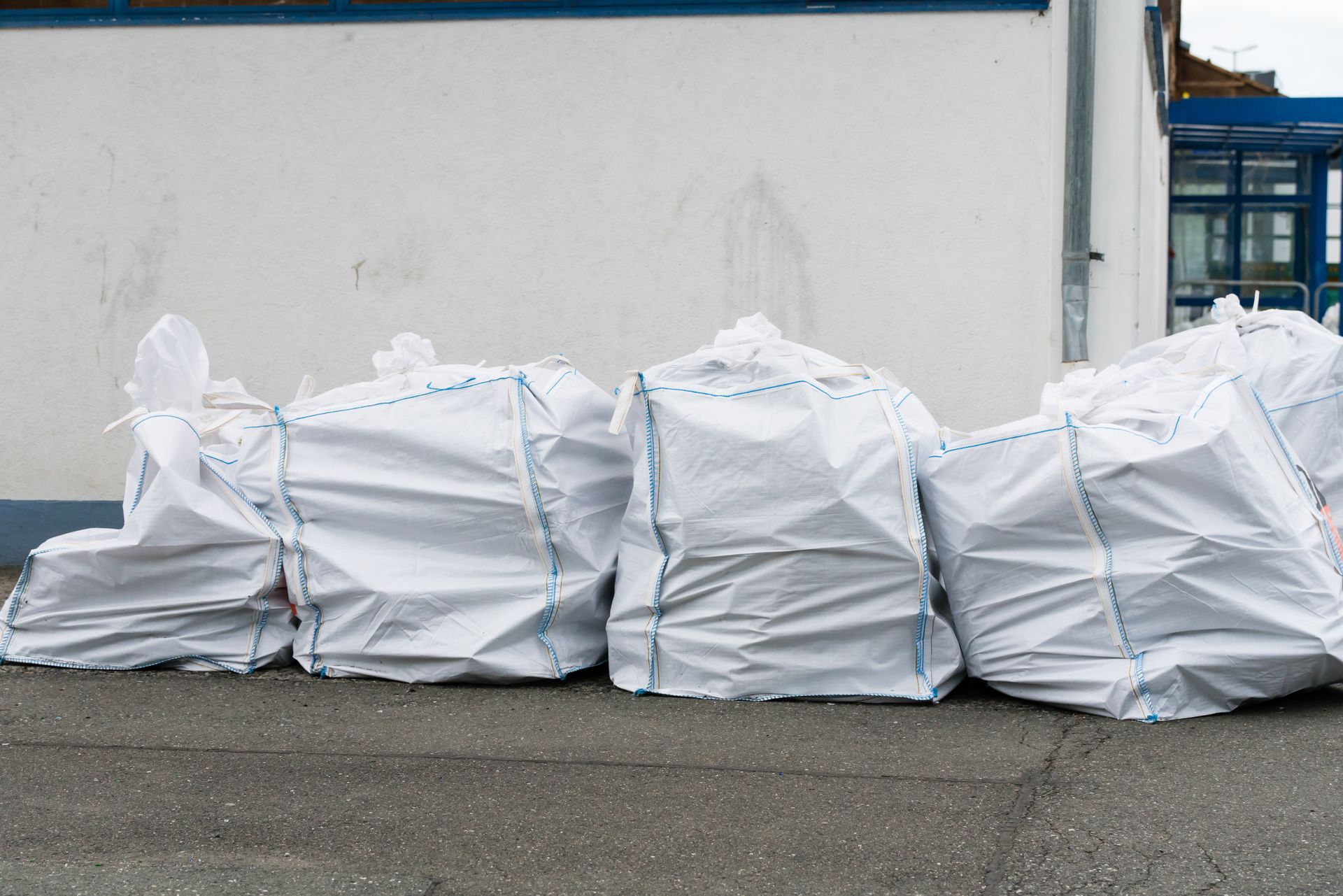 Des grands sacs blancs fermés, alignés contre un mur sur le trottoir.