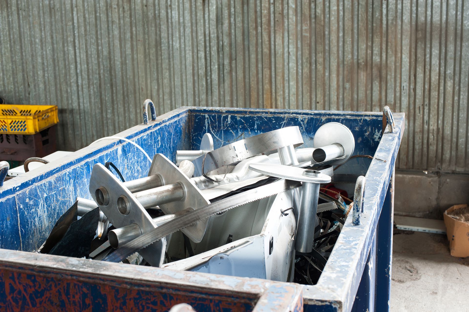 Une benne bleue chargée de divers déchets métalliques.