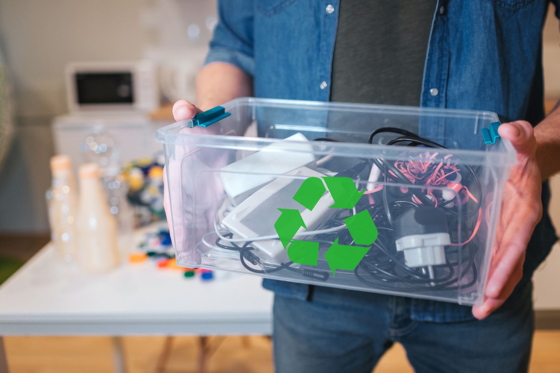 Une personne tient une boîte transparente avec un symbole de recyclage vert et divers appareils électroniques à l'intérieur.