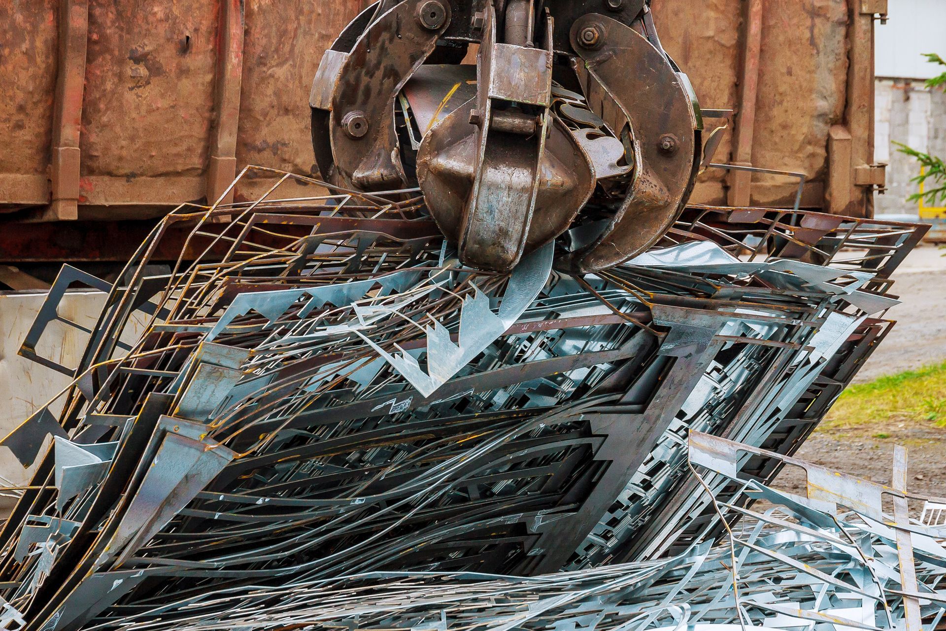 Des débris métalliques broyés sont entassés sous une pince hydraulique dans une zone industrielle.