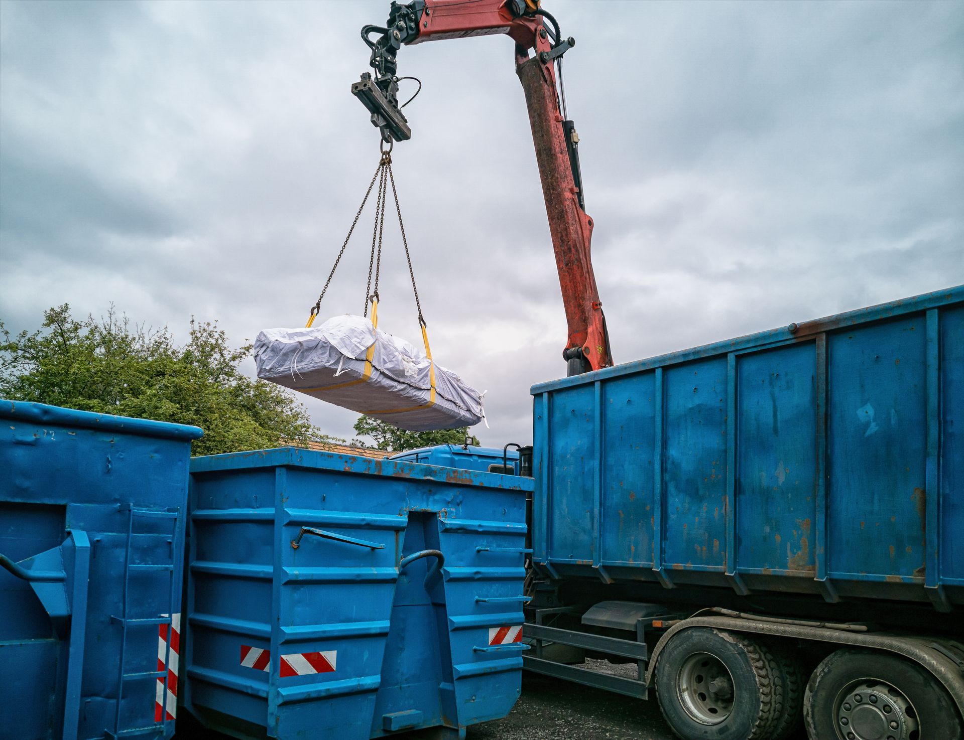 Une grue soulève un chargement emballé au-dessus de bennes bleues.