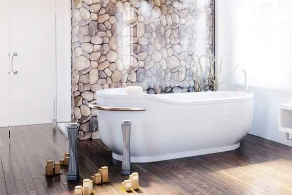 Freistehende weiße Badewanne in einem modernen Badezimmer mit Steinwandakzenten und Holzboden.