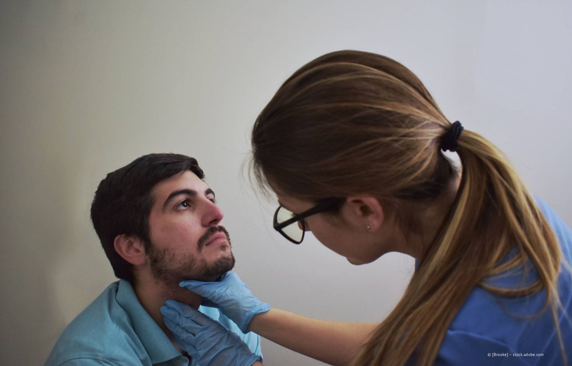 Medizinische Fachkraft untersucht den Hals eines Patienten mit behandschuhten Händen. Der Patient blickt nach oben.