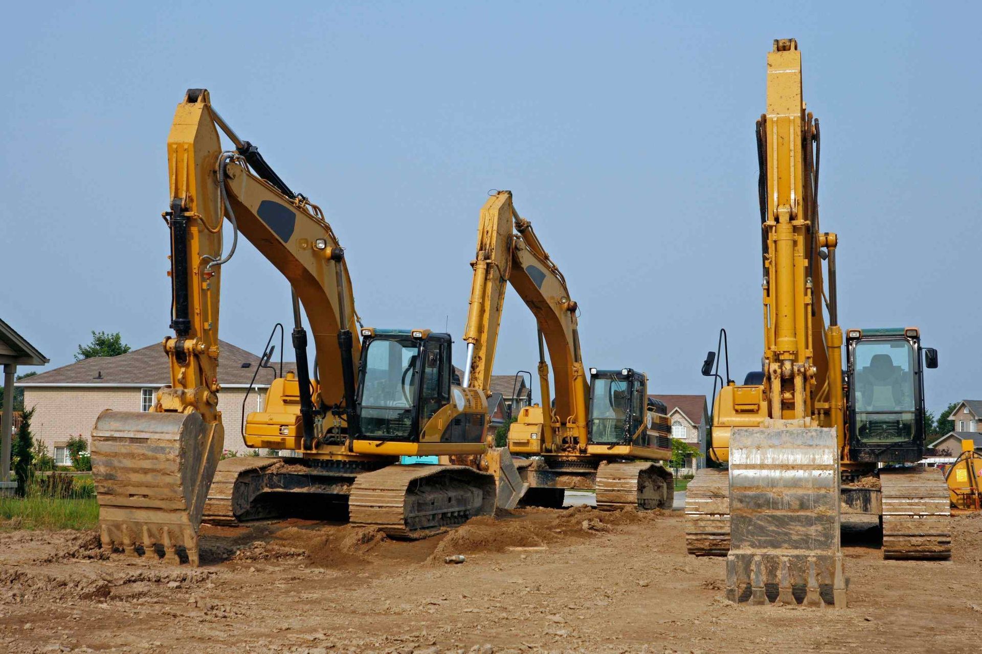 Tres excavadoras amarillas están estacionadas en un campo de tierra.