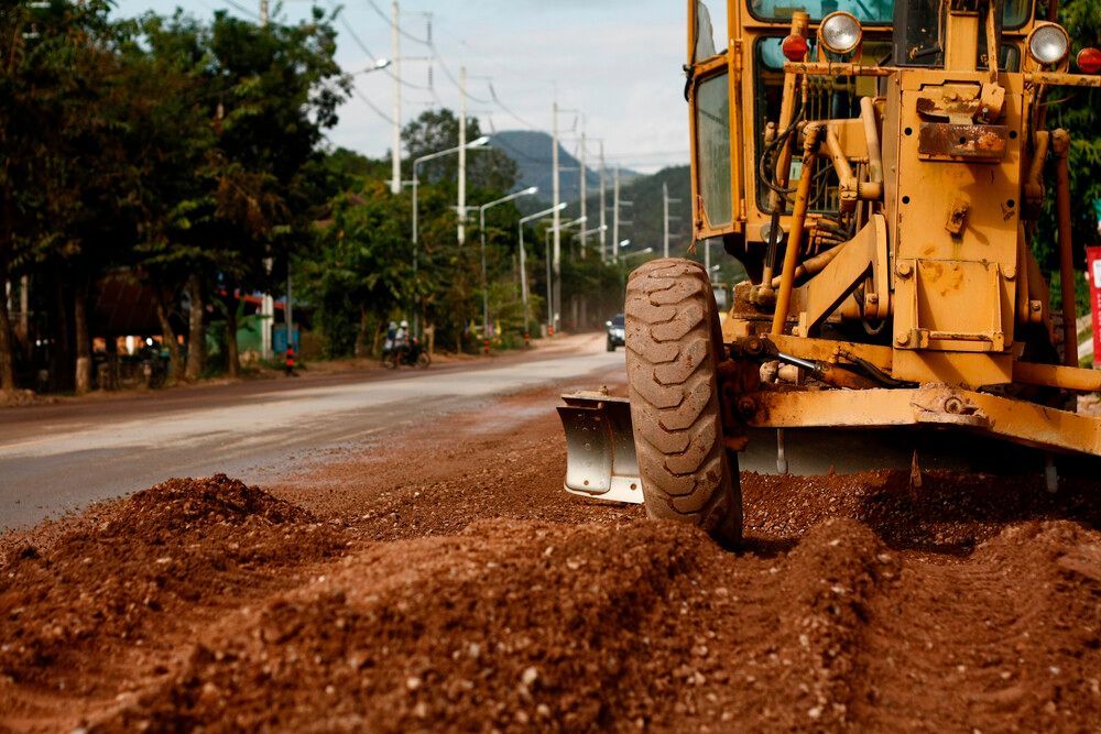 Una excavadora está moviendo tierra al costado de una carretera.