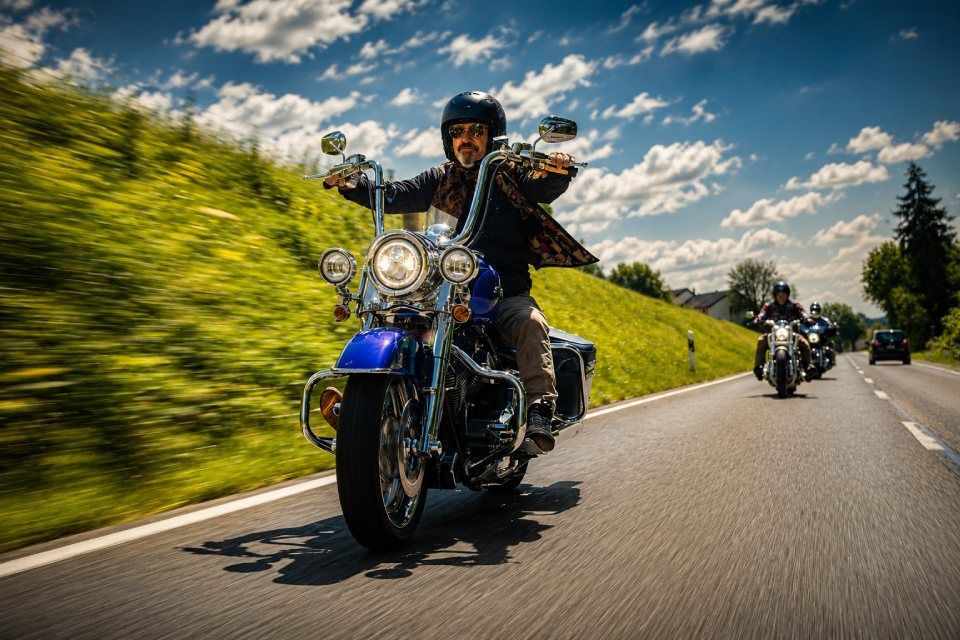 Ein Motorradfahrer in schwarzer Kleidung fährt auf einem blauen Motorrad auf einer kurvenreichen Strasse.