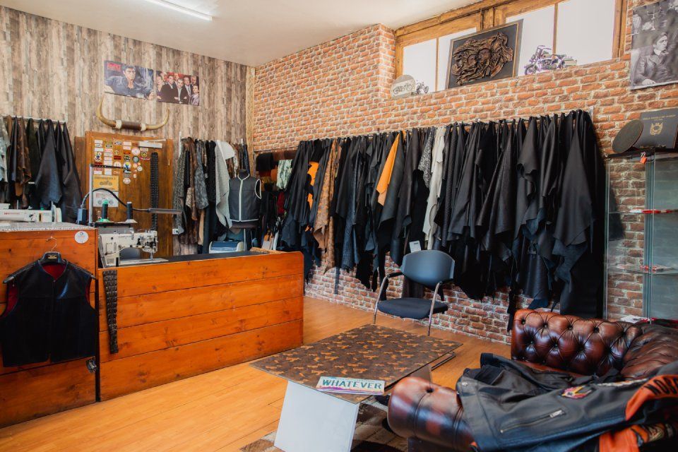 Eine Bekleidungsboutique mit Kleiderständern voller dunkler Kleidungsstücke, Holztheken und einem gepolsterten Sessel.