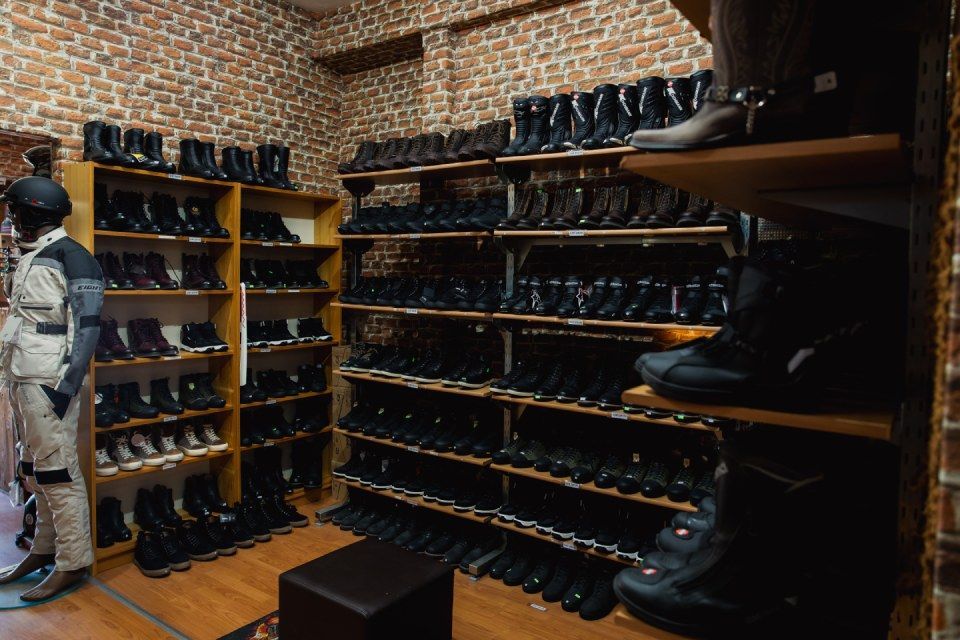 Reihen schwarzer Schuhe auf Holzregalen in einem Laden mit Backsteinwänden, links daneben steht eine Person.