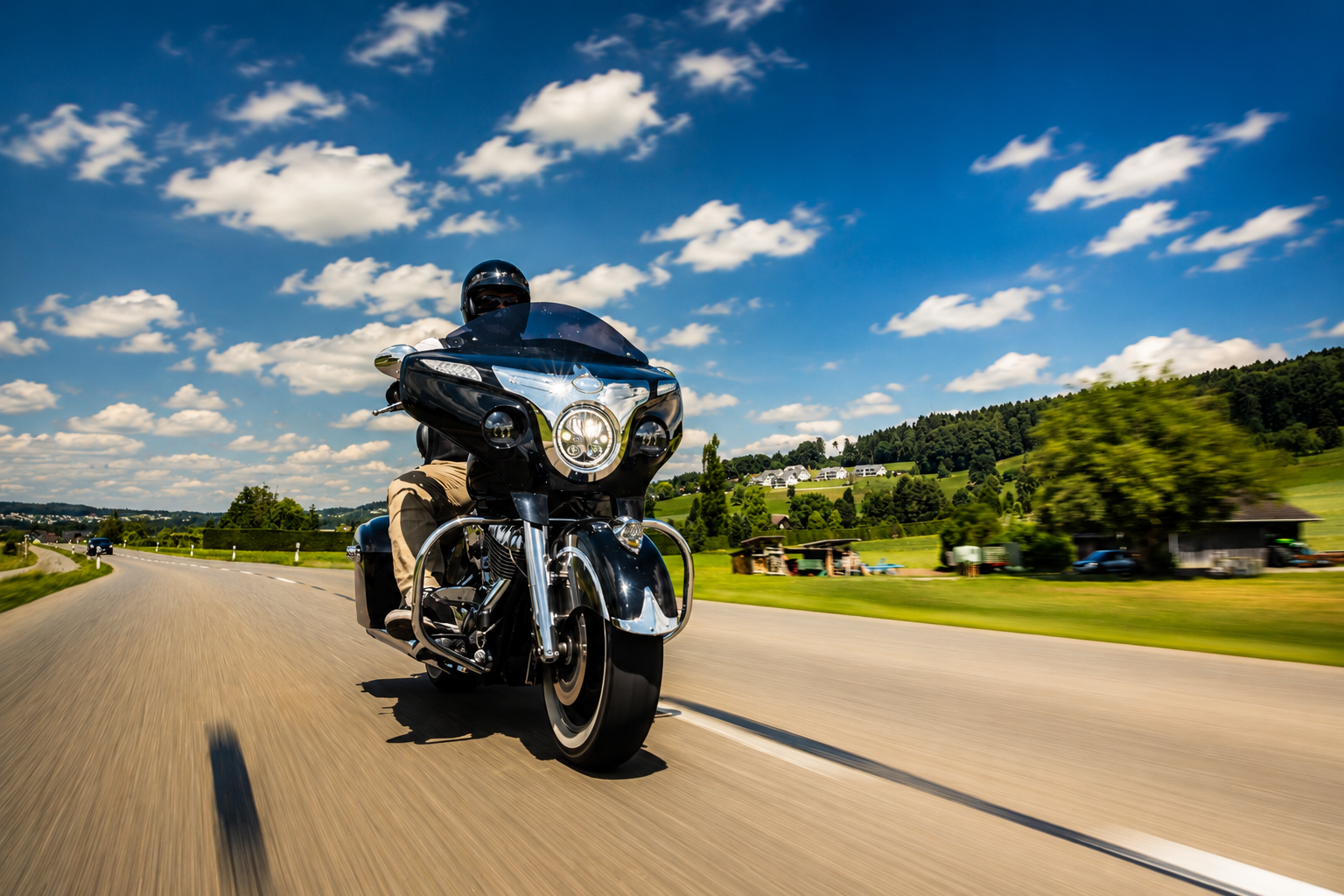 Ein Motorradfahrer fährt auf einem schwarzen Tourenmotorrad auf einer sonnigen Autobahn bei blauem Himmel und Wolken.
