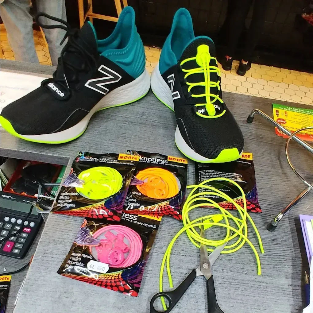 Zapatillas New Balance negras y turquesas con cordones amarillo neón, rodeadas de materiales para manualidades y alicates.