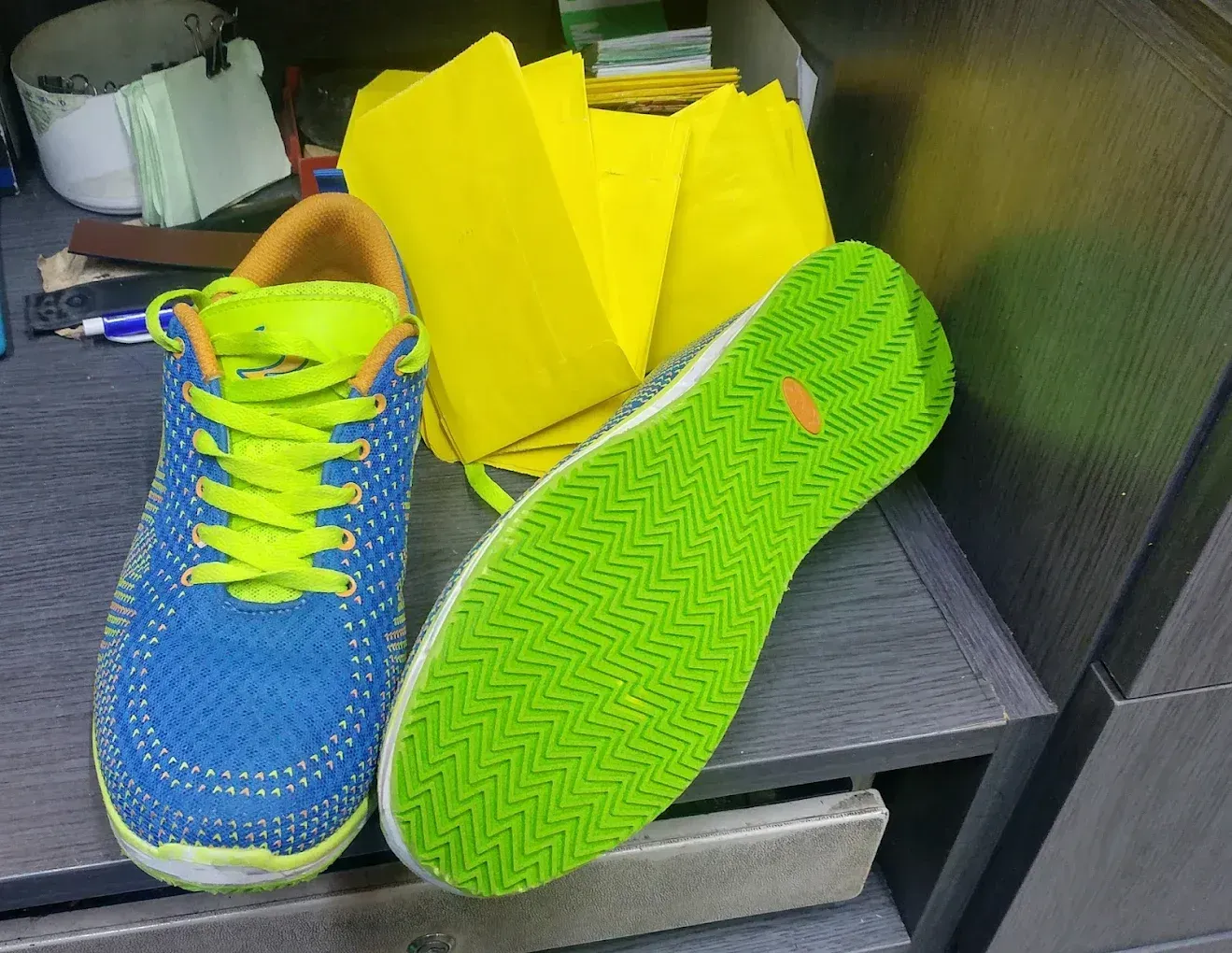 Una zapatilla de correr azul y verde neón junto a una suela de zapato verde neón y papel de seda amarillo en un estante.