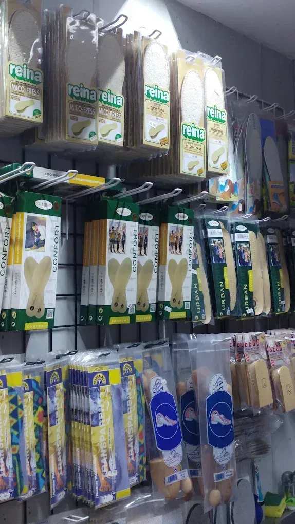 Exhibición en tienda de artículos domésticos empaquetados y colgados en bolsas de plástico, en su mayoría blancas y azules, en un estante de pared.