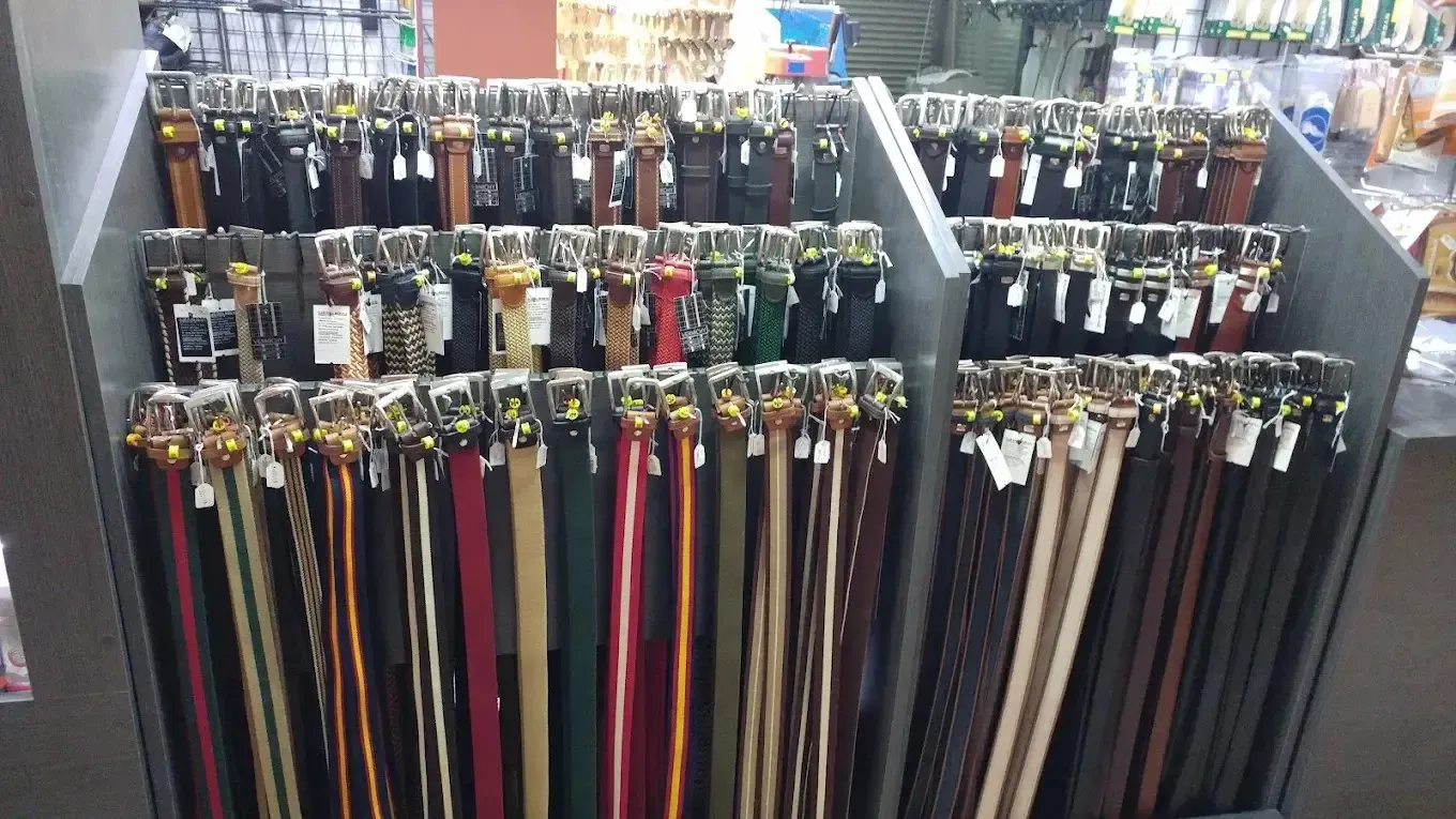 Filas de cinturones de colores exhibidos verticalmente en un estante de la tienda.