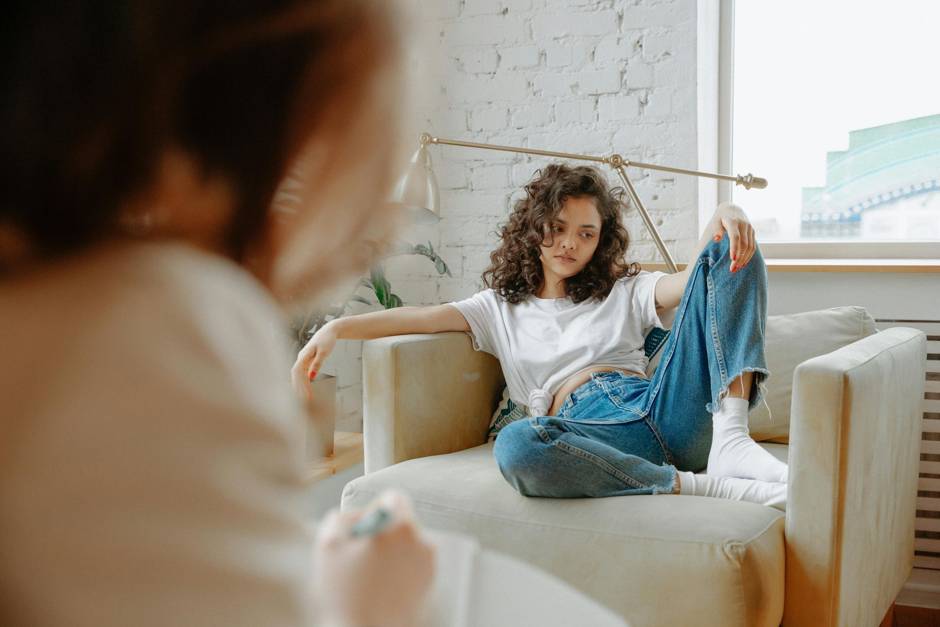 Una persona se relaja en un sillón en una habitación luminosa, sonriendo y con una pierna levantada.