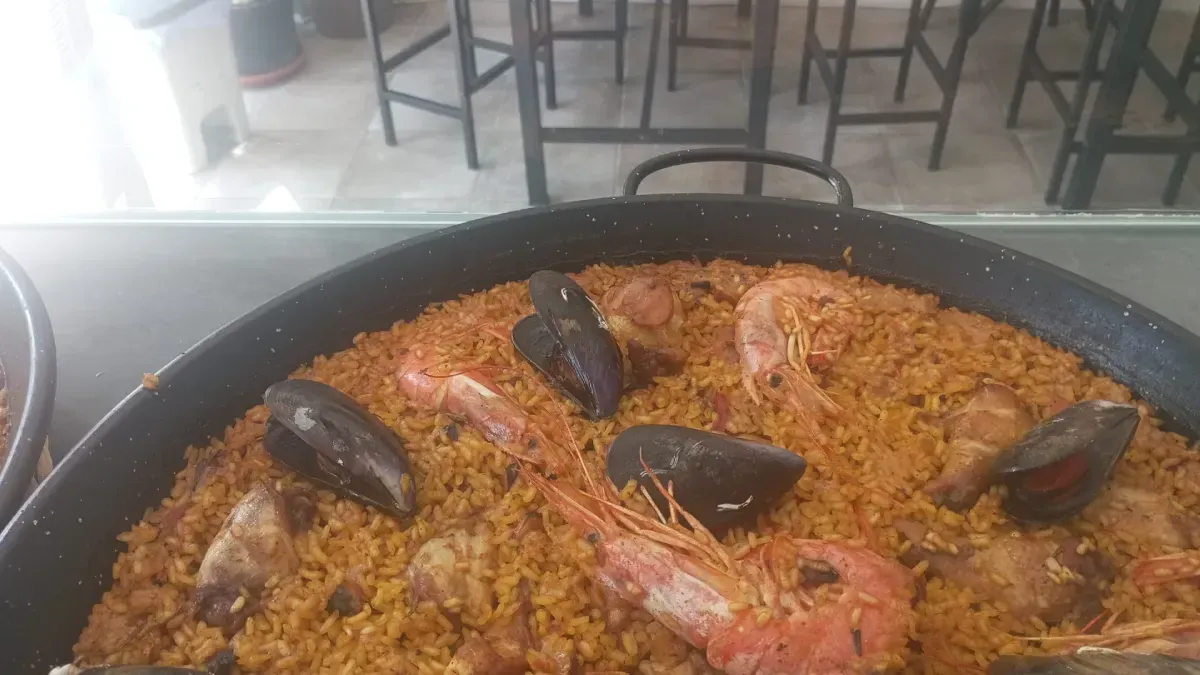 Plato redondo de arroz horneado cubierto con hierbas, rodajas de limón y pescado sobre una mesa.