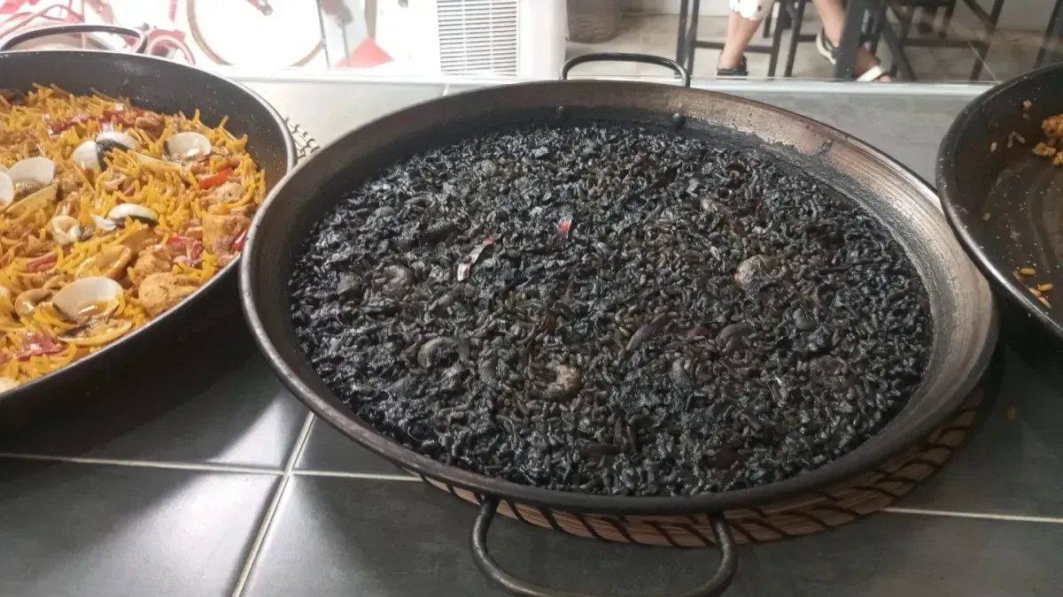 Paella de marisco con gambas, calamares y rodajas de limón en una sartén negra.