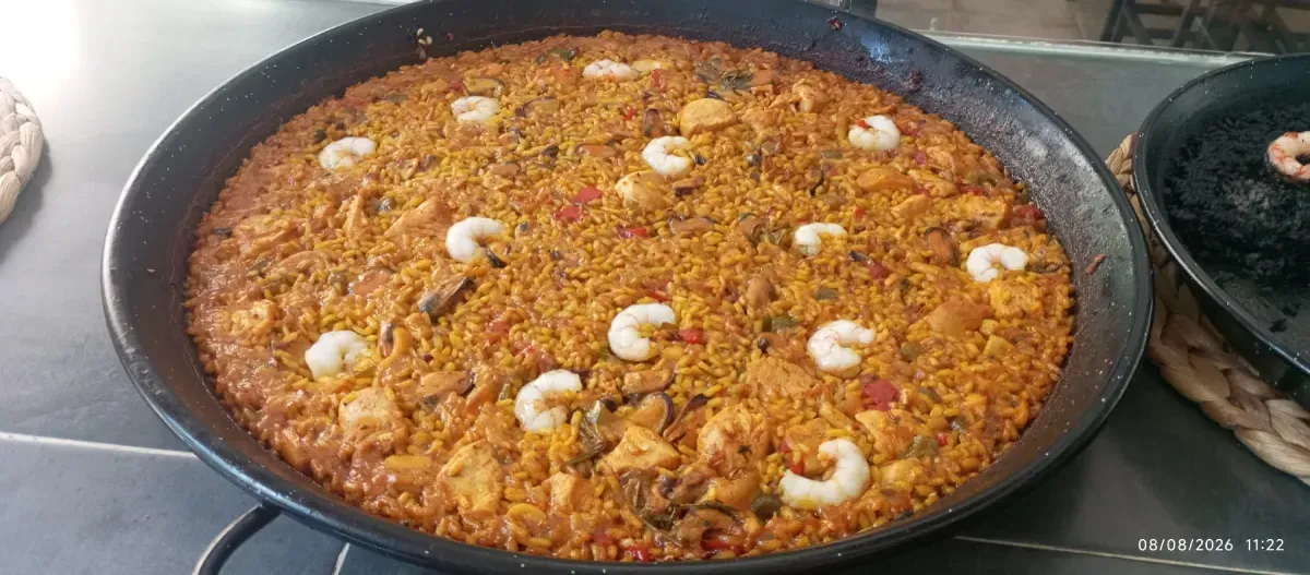 Plato redondo de arroz horneado cubierto con hierbas, rodajas de limón y pescado sobre una mesa.