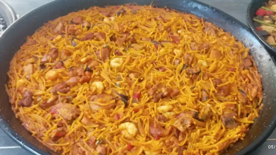 Una olla grande de arroz naranja mezclado con verduras ralladas y trozos de carne.