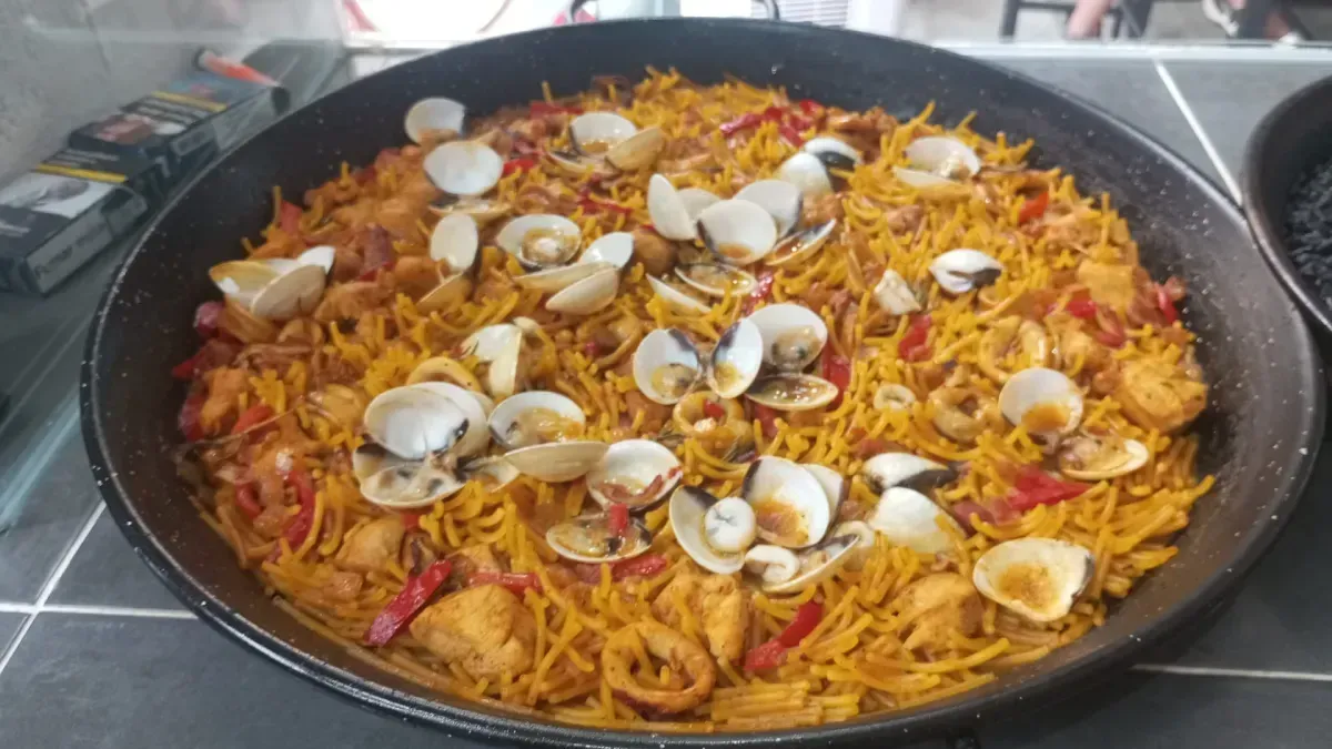 Una olla grande de arroz naranja mezclado con verduras ralladas y trozos de carne.