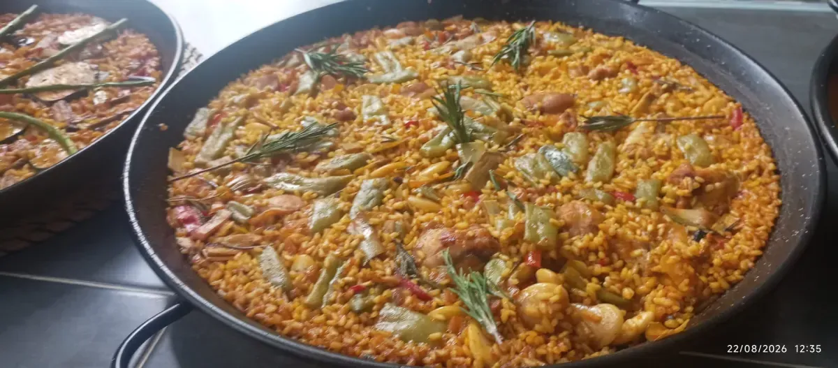 Grandes sartenes de arroz amarillo con mariscos en una mesa de buffet.