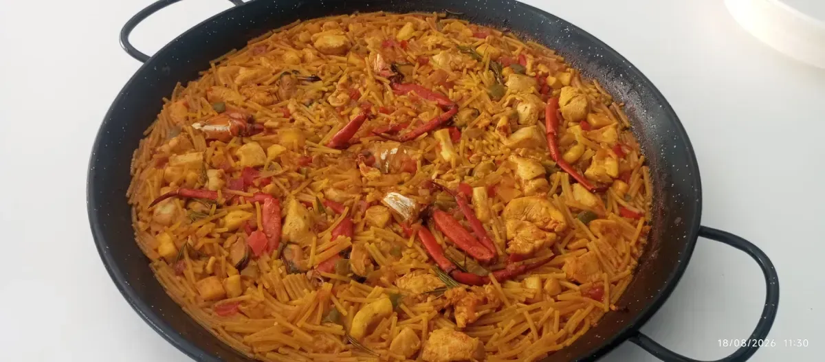Una olla grande de arroz naranja mezclado con verduras ralladas y trozos de carne.