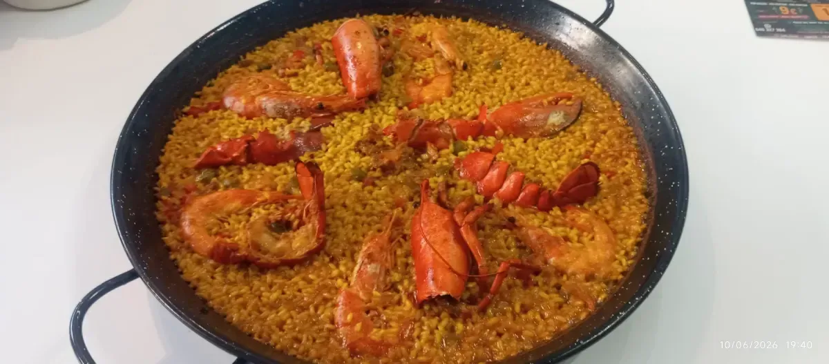 Sartén de paella de langosta con trozos de langosta de color rojo brillante dispuestos sobre arroz.