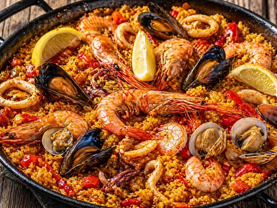 Paella de marisco en sartén, cubierta con gambas, mejillones, almejas, calamares y rodajas de limón.