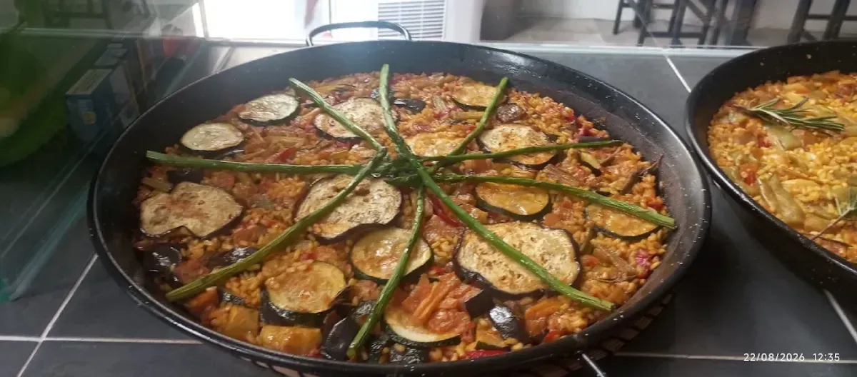 Grandes paelleras con arroz, mariscos y judías verdes cocinándose en una cocina.