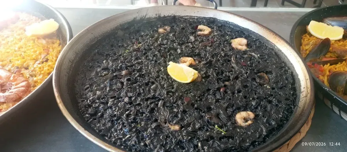 Una gran fuente de arroz negro cubierta con rodajas de limón, flanqueada por bandejas de comida colorida.