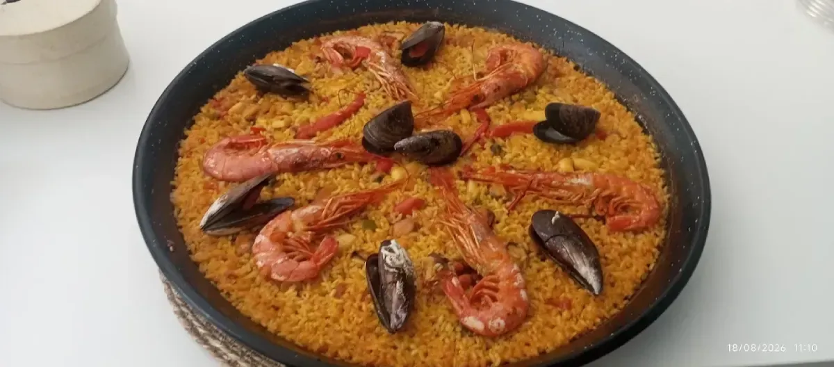 Paella de marisco en una sartén negra, cubierta con gambas y mejillones sobre una mesa blanca.