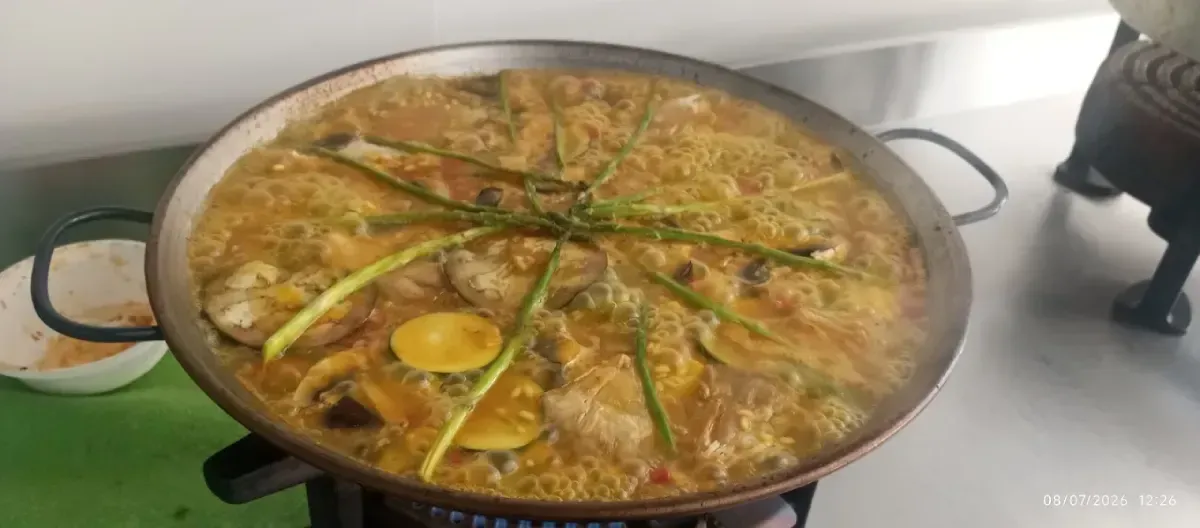 Una paella de mariscos grande hirviendo a fuego lento con rodajas de limón y judías verdes en la estufa.
