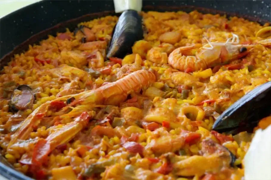 Paella de arroz con azafrán, gambas y mejillones, servida con pinzas.