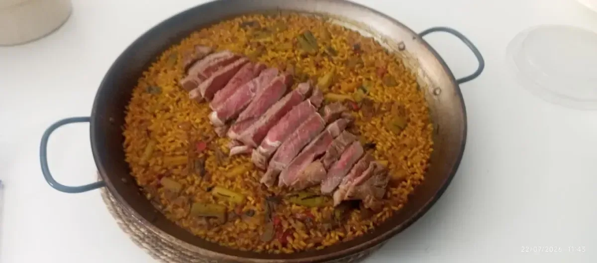 Carne en rodajas sobre una paellera o una paella, vista desde arriba.
