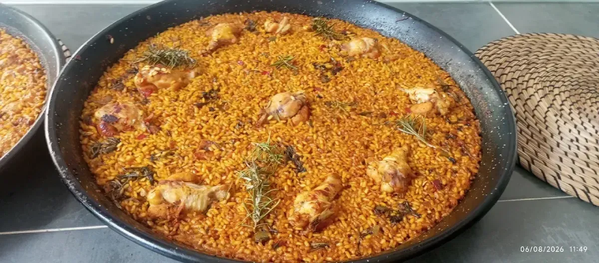 Una fuente poco profunda de arroz naranja con trozos de pollo, junto a una cesta de mimbre sobre una mesa.