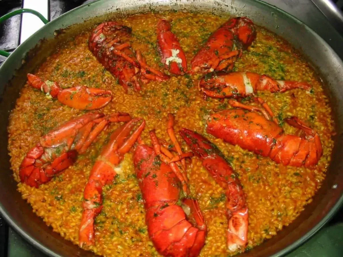 Sartén de paella de langosta con trozos de langosta de color rojo brillante dispuestos sobre arroz.